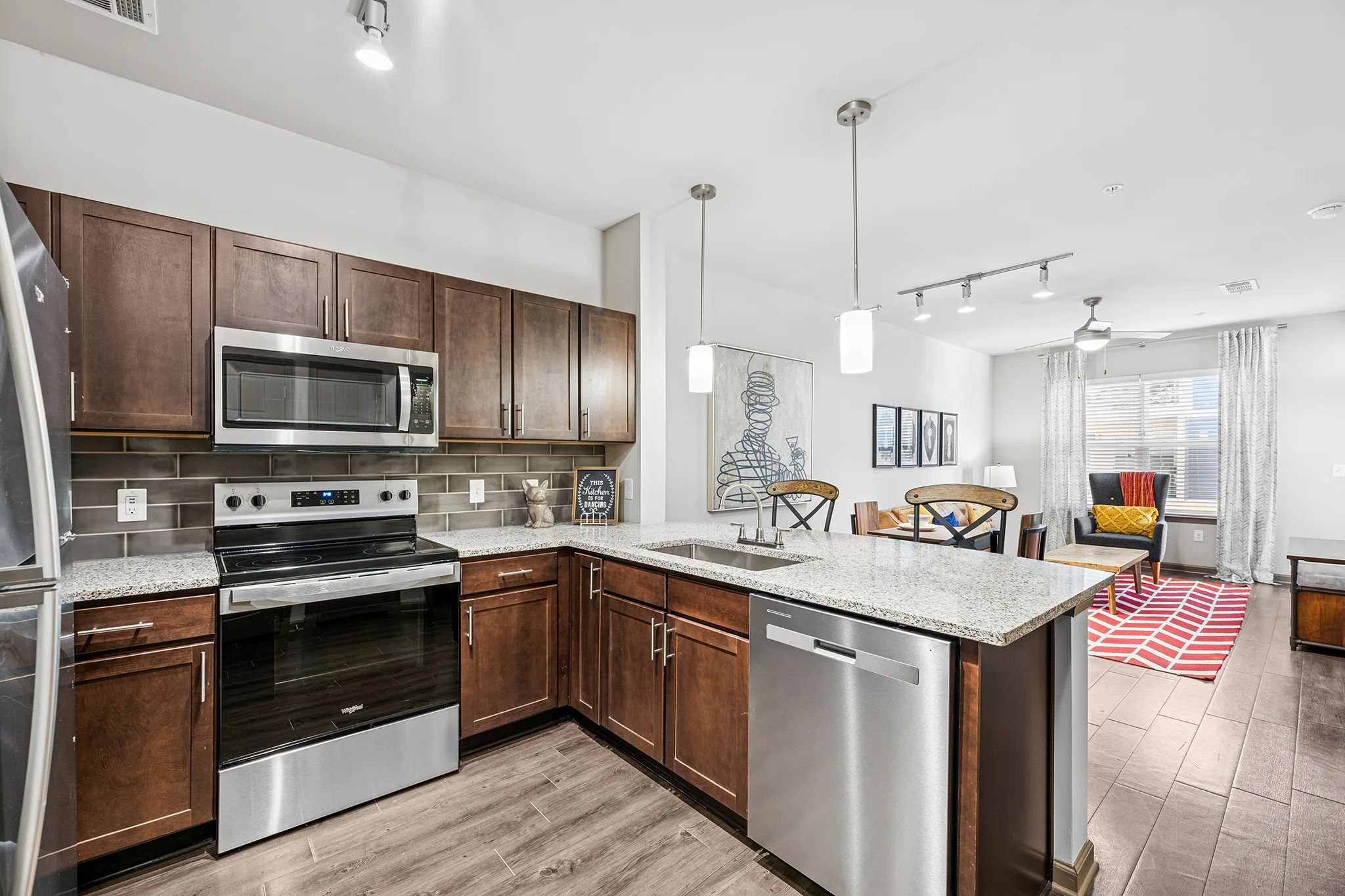 A modern kitchen featuring dark wood cabinets, stainless appliances, and a peninsula opening to the living room.